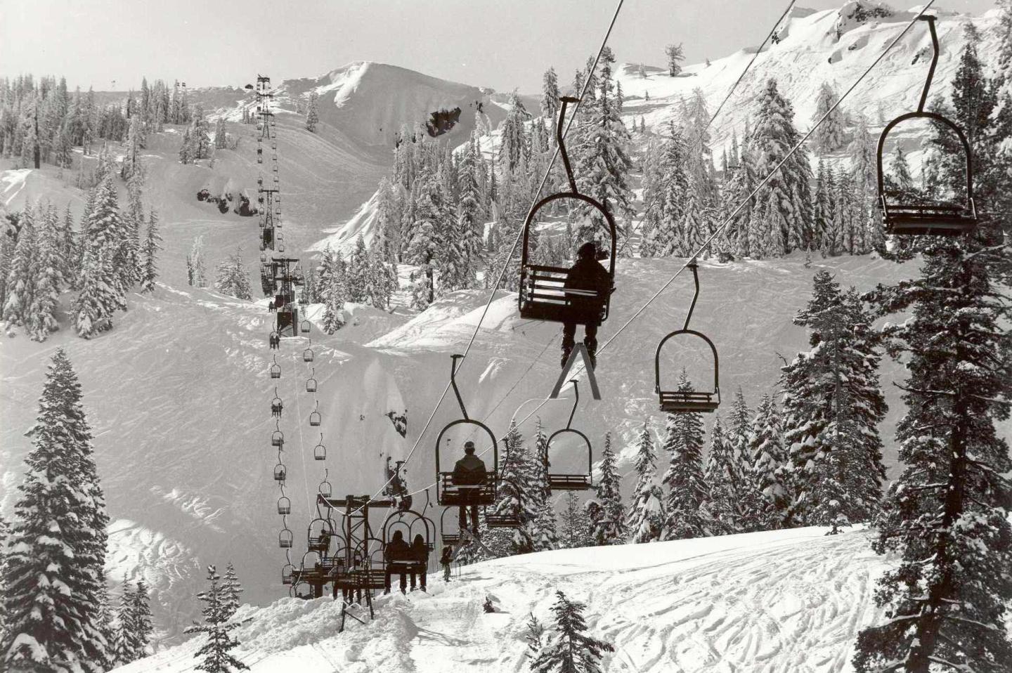 Skiers ride a snowy mountain chairlift among snow-covered trees.