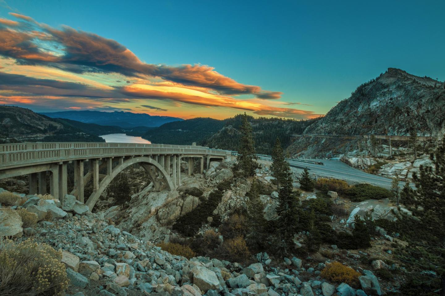 Rainbow Bridge Truckee over rocky landscape at sunset, with colorful clouds and distant mountains.