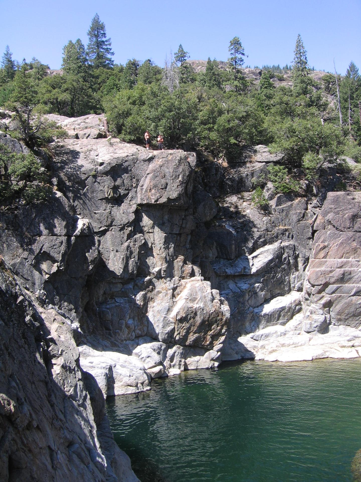 Emerald Pools - Rocky cliff with green trees above a serene lake.