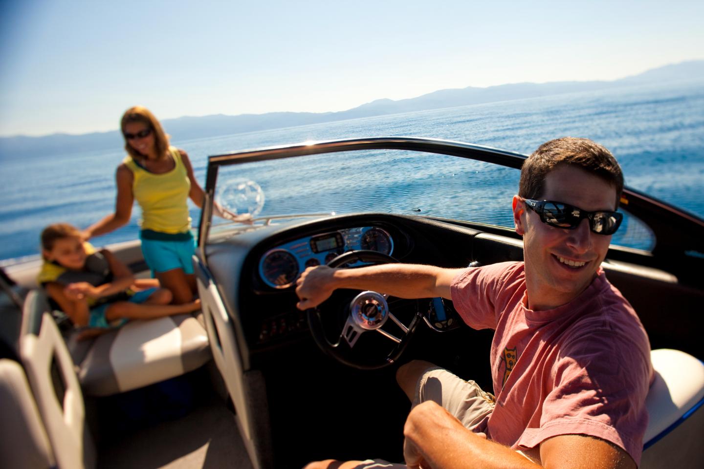 Man steering a boat with two passengers, smiling under a sunny sky.