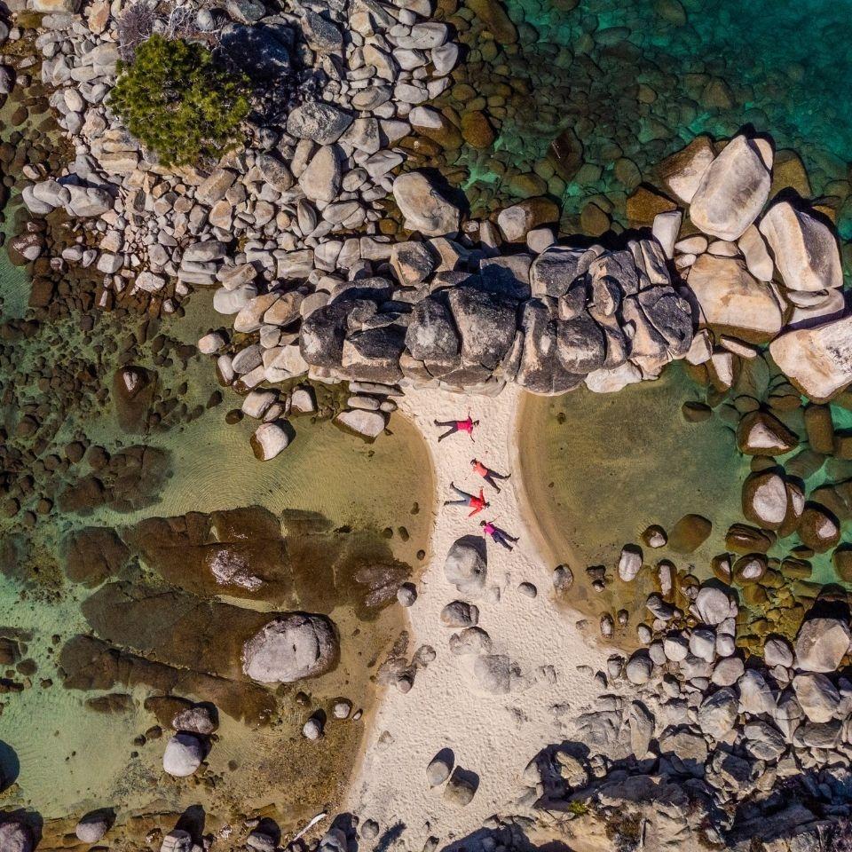 Three people in red on rocky beach with clear water.