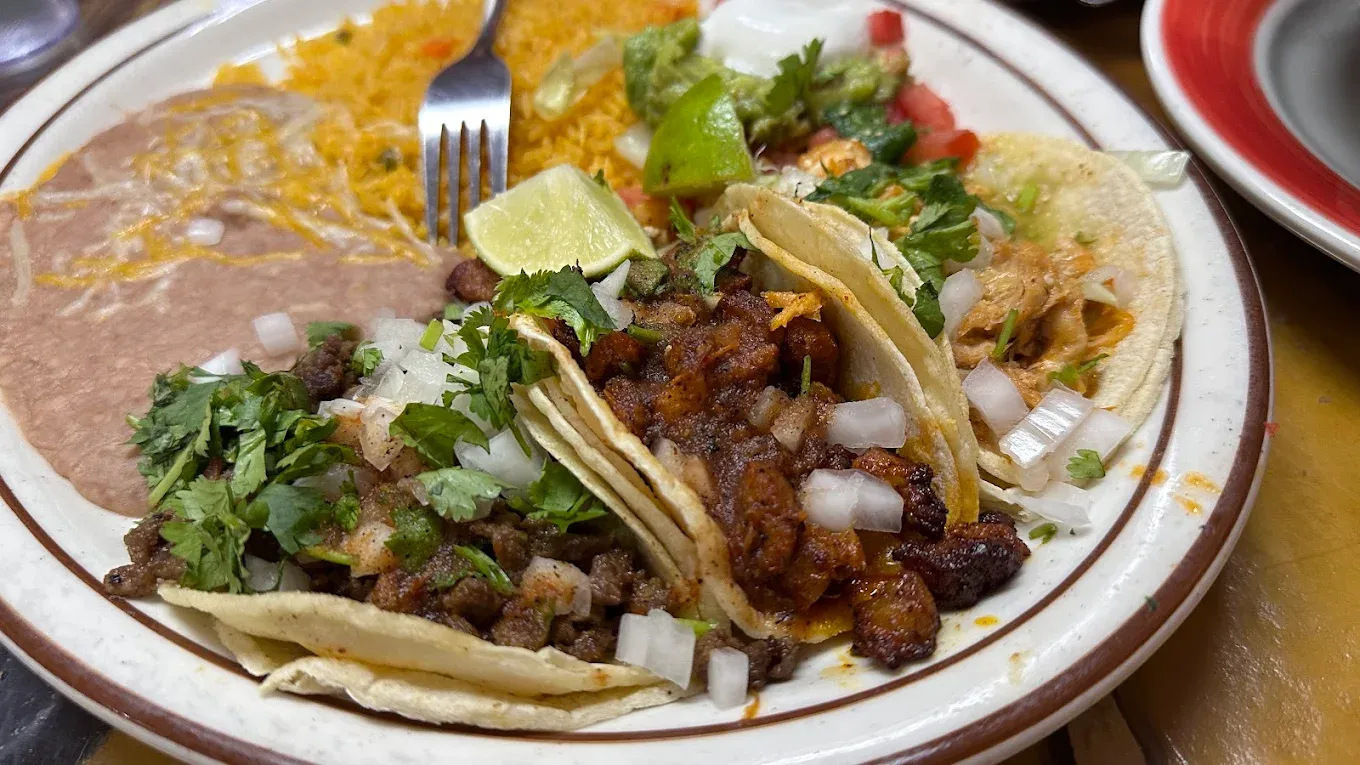 Tacos with diced onions, cilantro, rice, beans, and salad on a white plate.