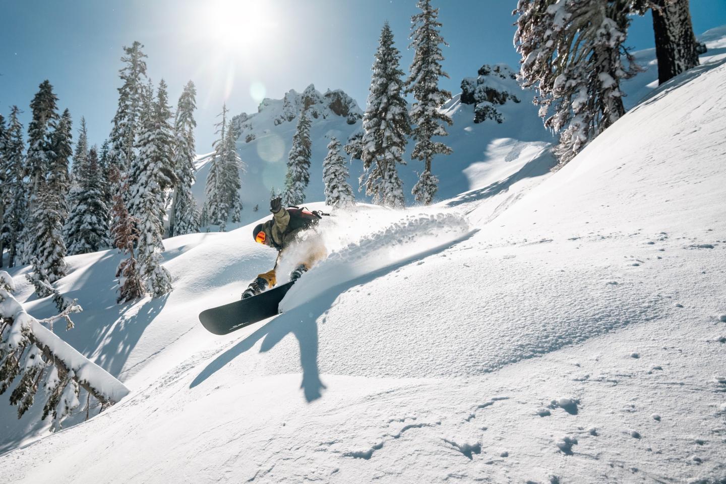 Snowboarder carving through fresh snow on a sunny, snowy mountain slope.