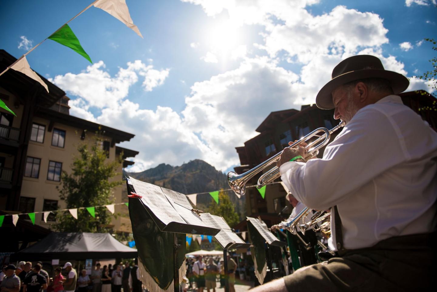 Man wearing a hat plays trumpet at outdoor festival under clear sky.