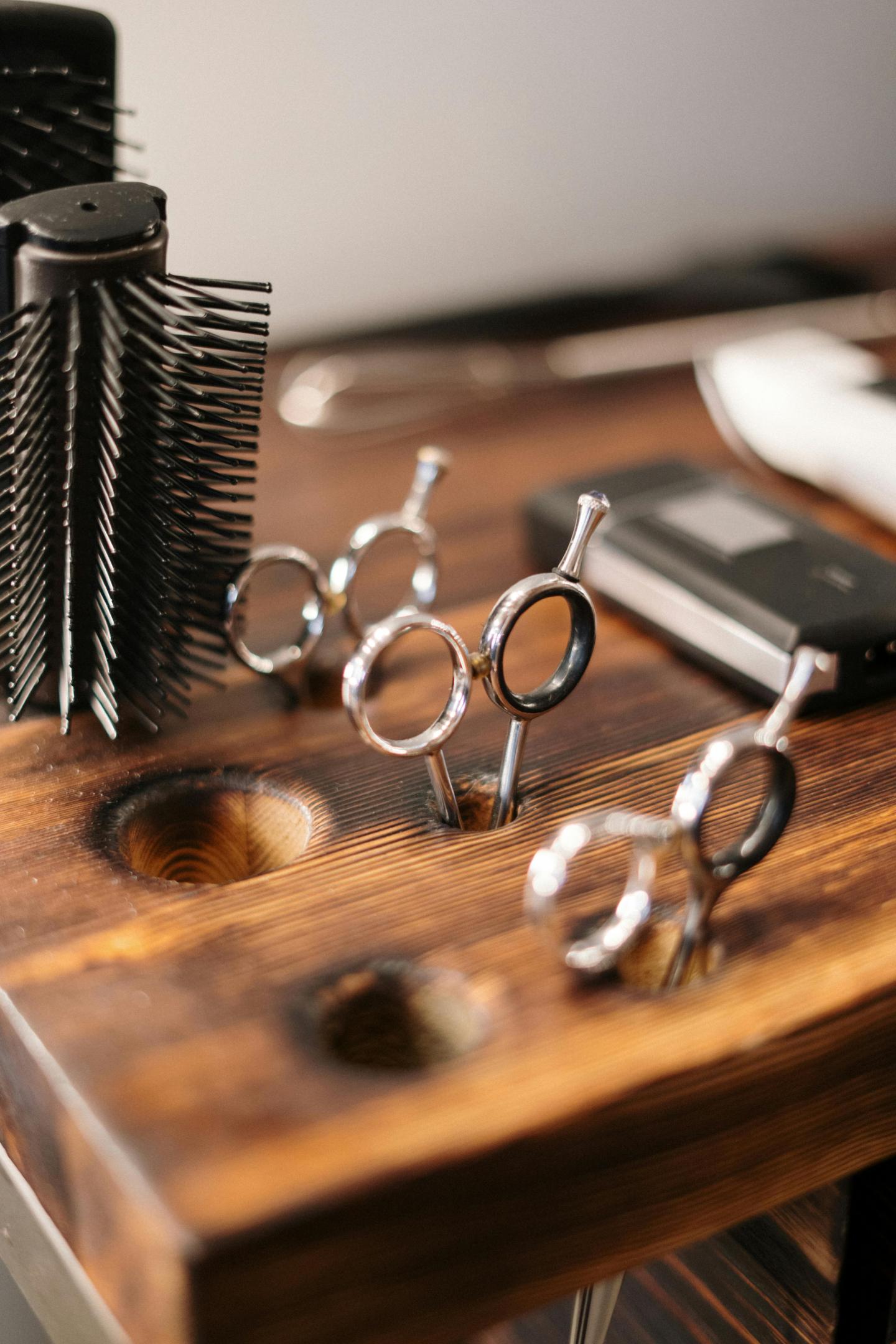 Hair salon tools on a wooden countertop, including scissors and a hairbrush.