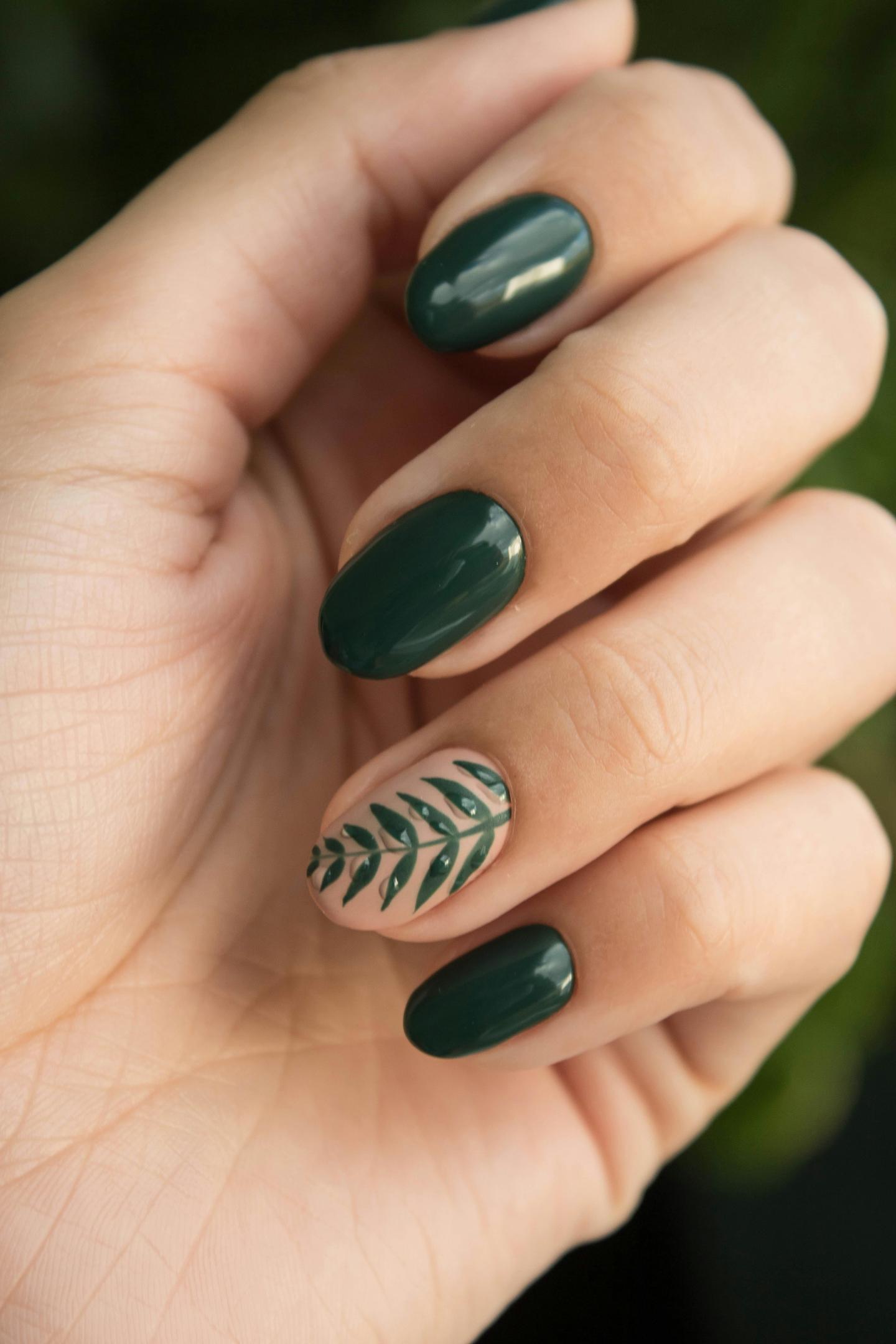 Dark green nails with a leaf design on the ring finger.