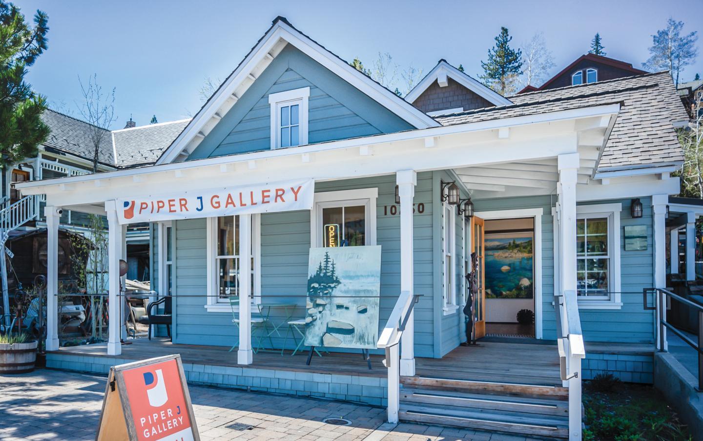 Blue house with a white porch, sign says "Gallery," trees in background.