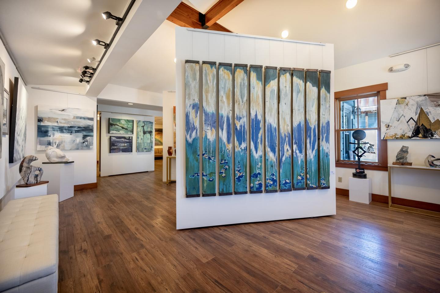 Art gallery with wooden floors, featuring abstract paintings and sculptures.