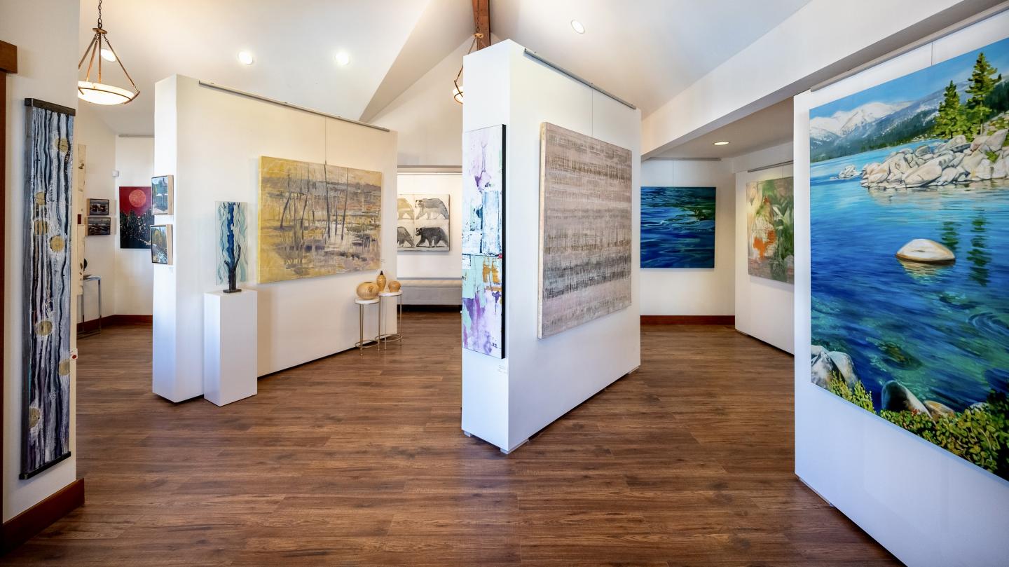 Art gallery with paintings on white walls, wooden floor, bright lighting.