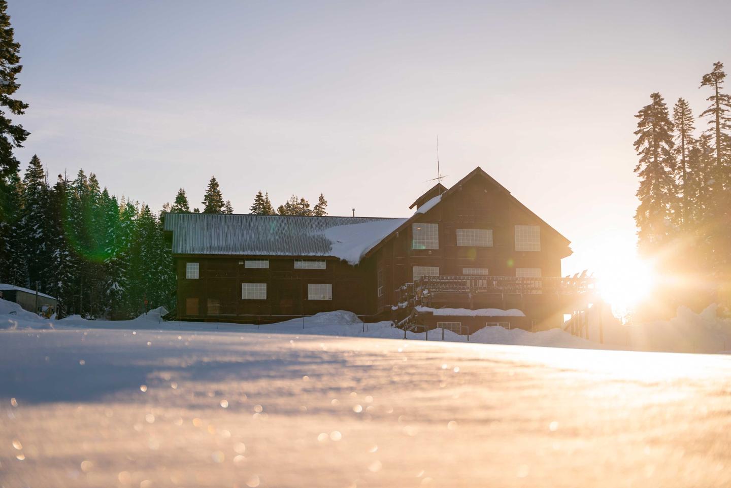 Snowy lodge at sunrise with trees in the background.