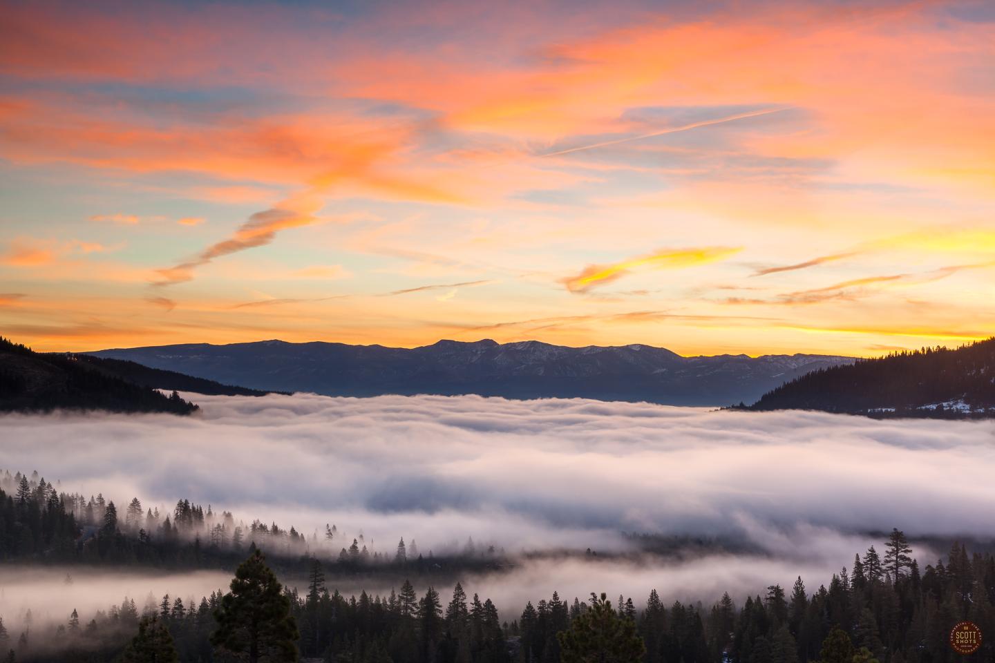 Sunset over a foggy valley with rolling hills and vibrant, colorful sky.