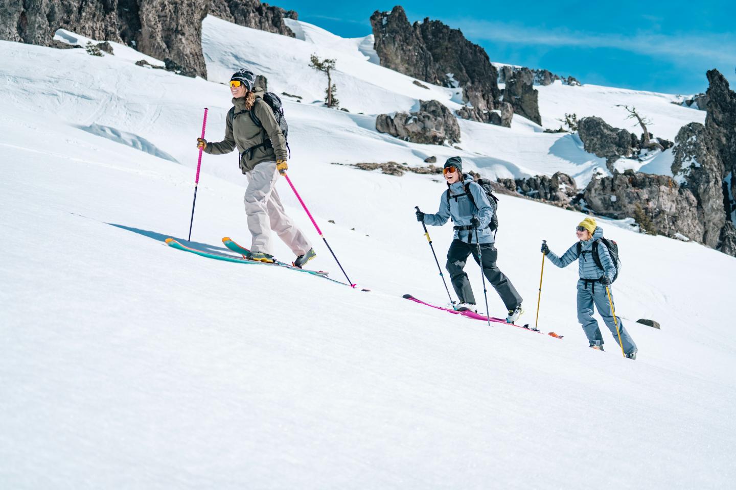 Three skiers ascending a snowy mountain slope under a blue sky.