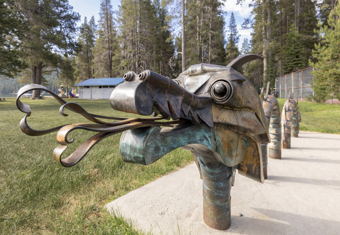 Dragon head sculpture in a park, trees and blue skies in the background.