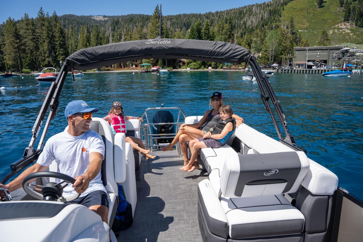 A family relaxes on a boat on a clear lake near forested hills.