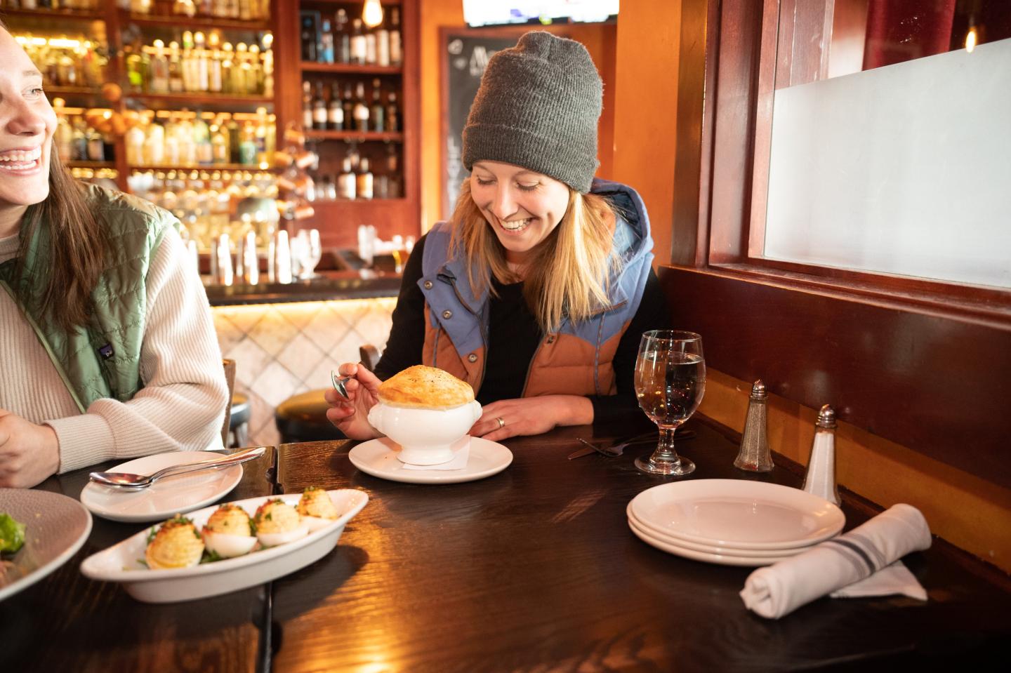 Woman smiling at soup in a cozy restaurant setting.