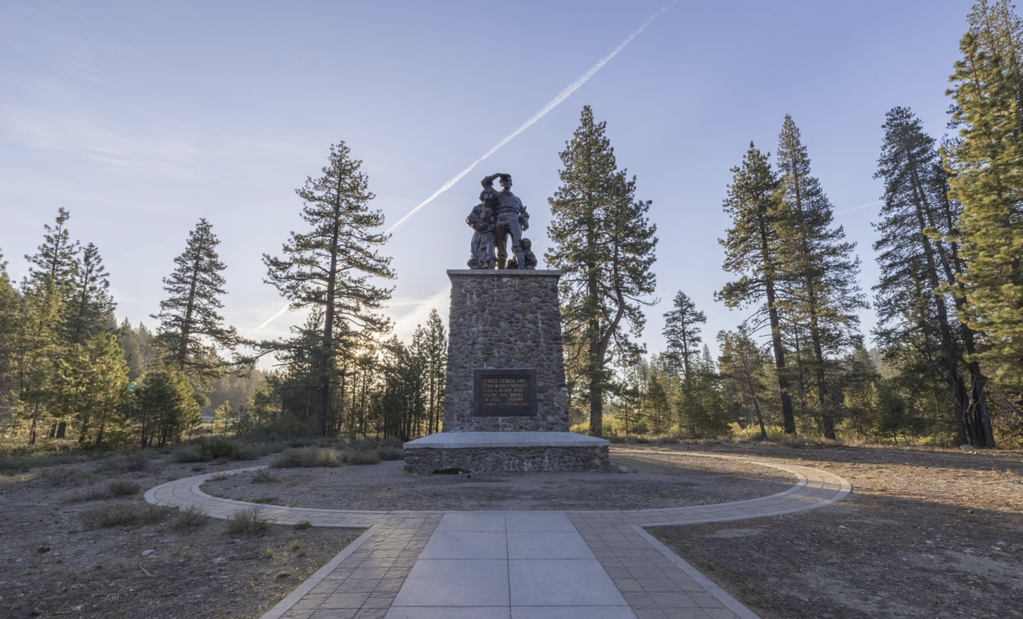 Monument surrounded by pine trees under a clear sky.