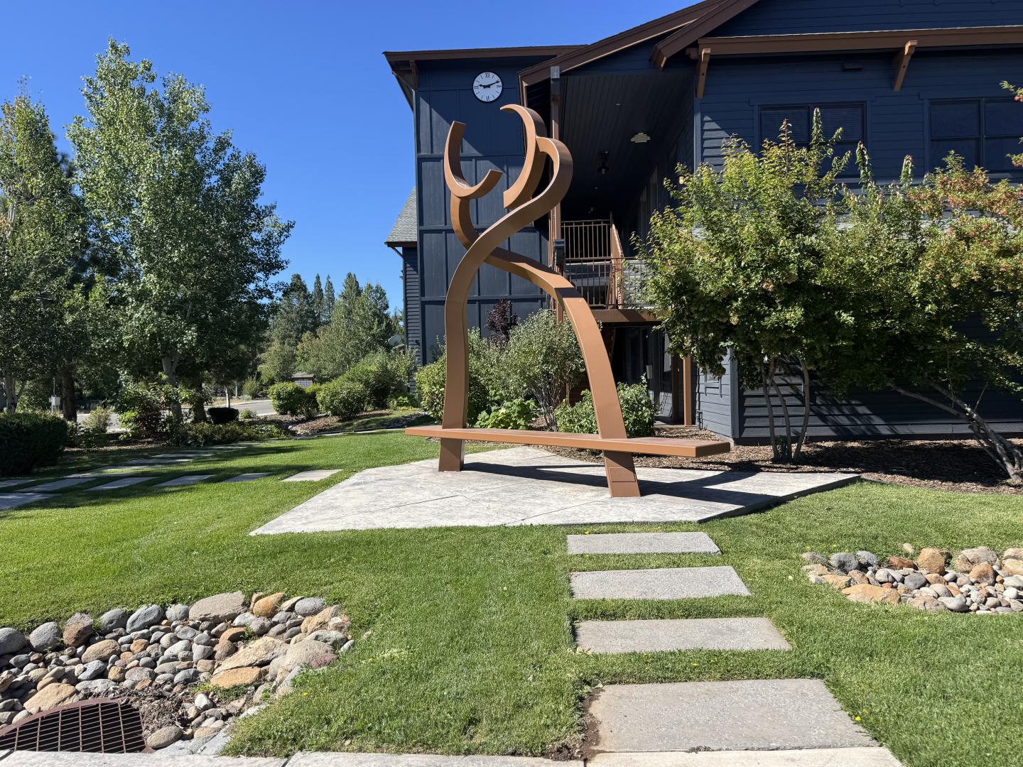 Modern metal sculpture on a lawn, near a building with blue siding.