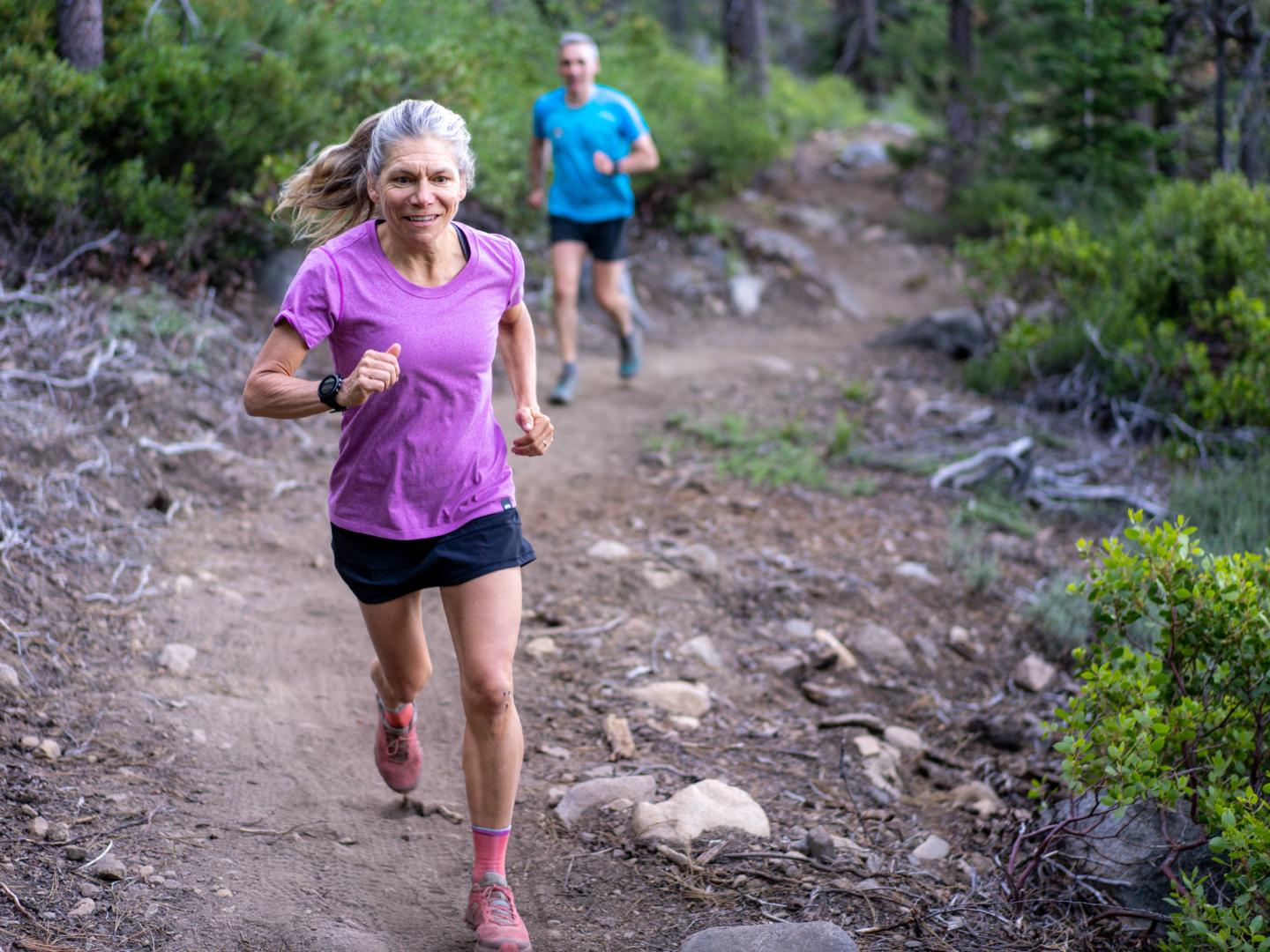 Two people trail running in a forest, wearing casual athletic gear.