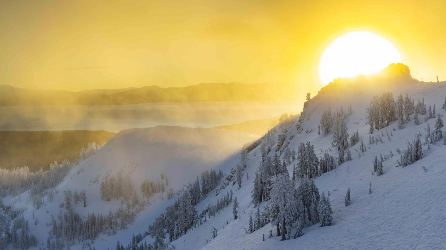 Snowy mountain landscape at sunrise, warm yellow glow over peaks.