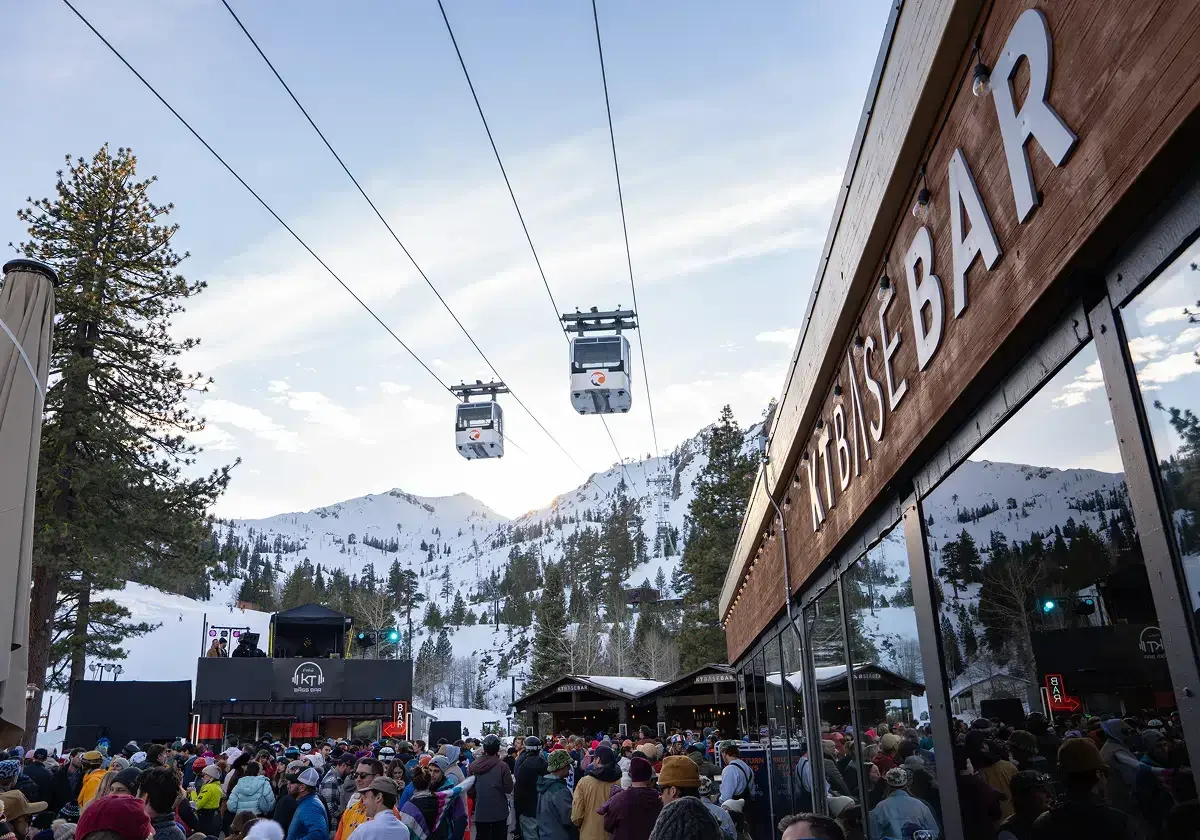 Ski resort with cable cars, mountains, and a crowd outside a bar.