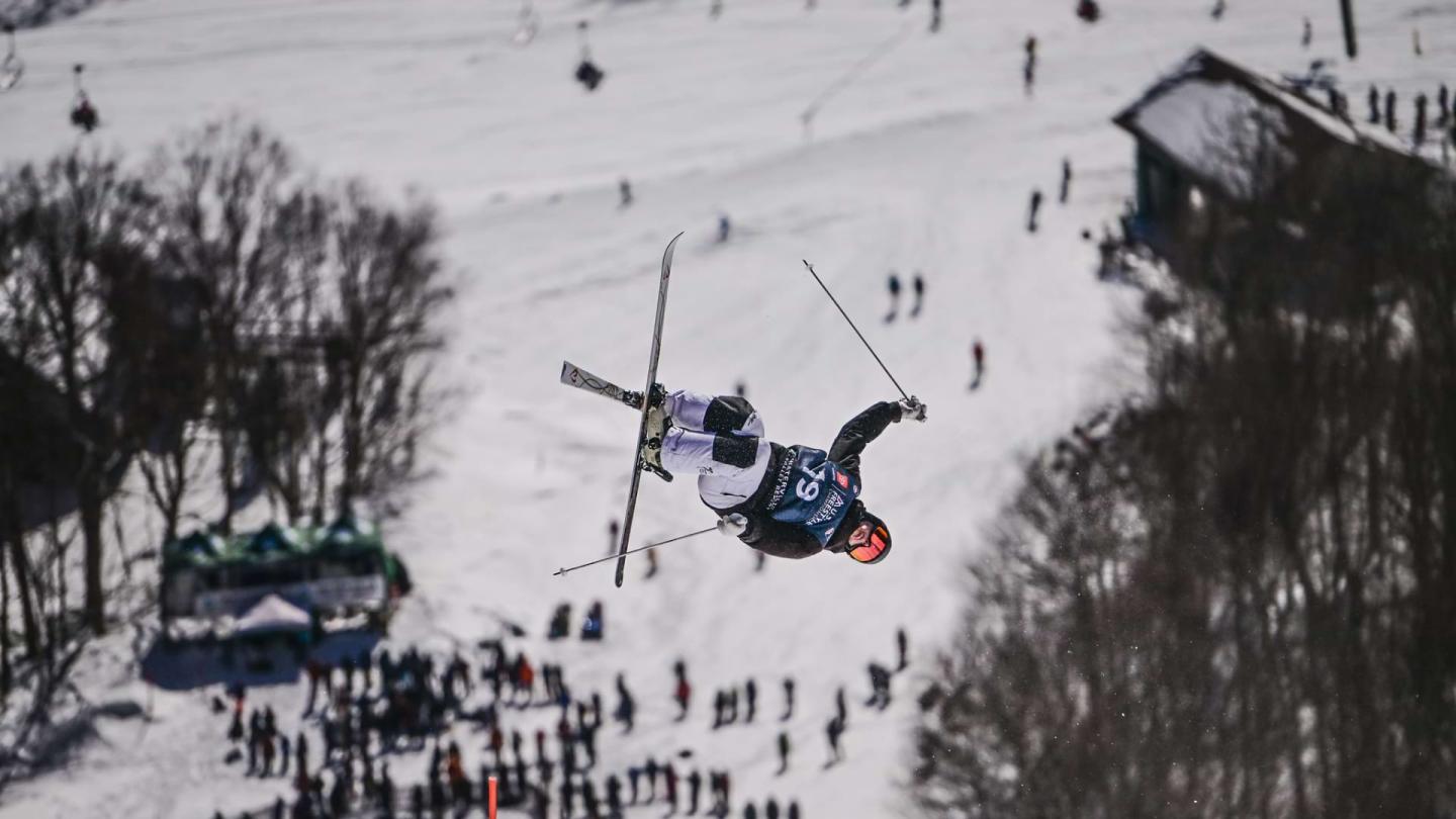 Skier airborne, surrounded by snow, with spectators below.