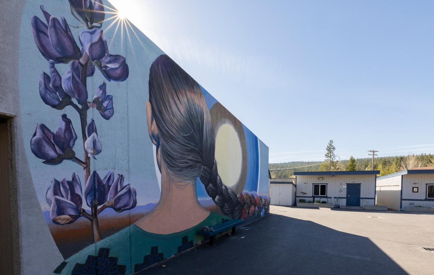 Mural of a woman with braided hair, purple flowers, and a large moon on a building wall.