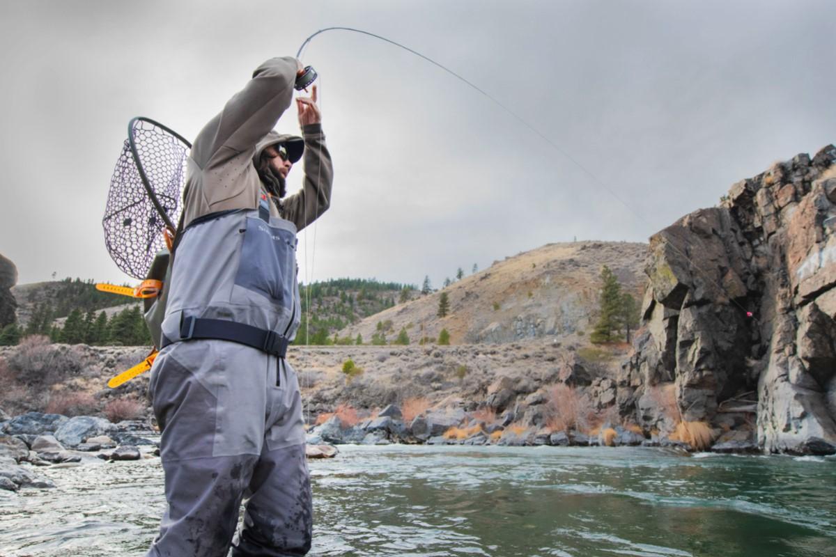 Angler fly fishing in a rocky river, holding a rod and net.
