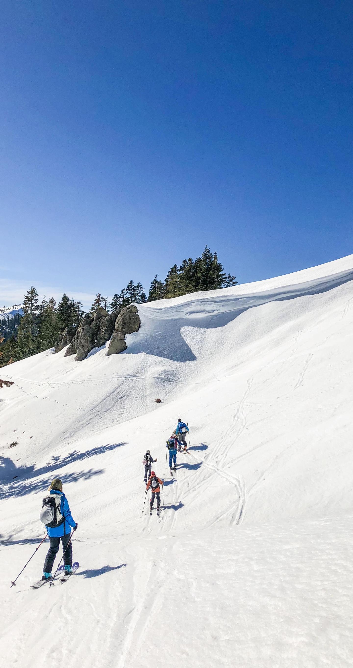 Skiers on a snowy slope under a clear blue sky.