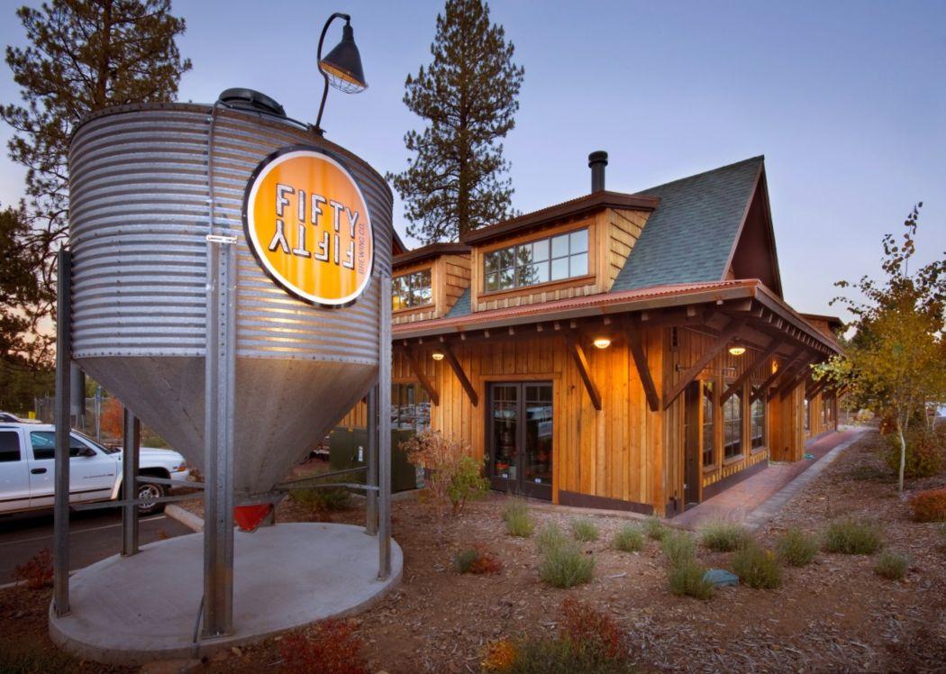 Brewery with metal silo and wooden building at dusk.