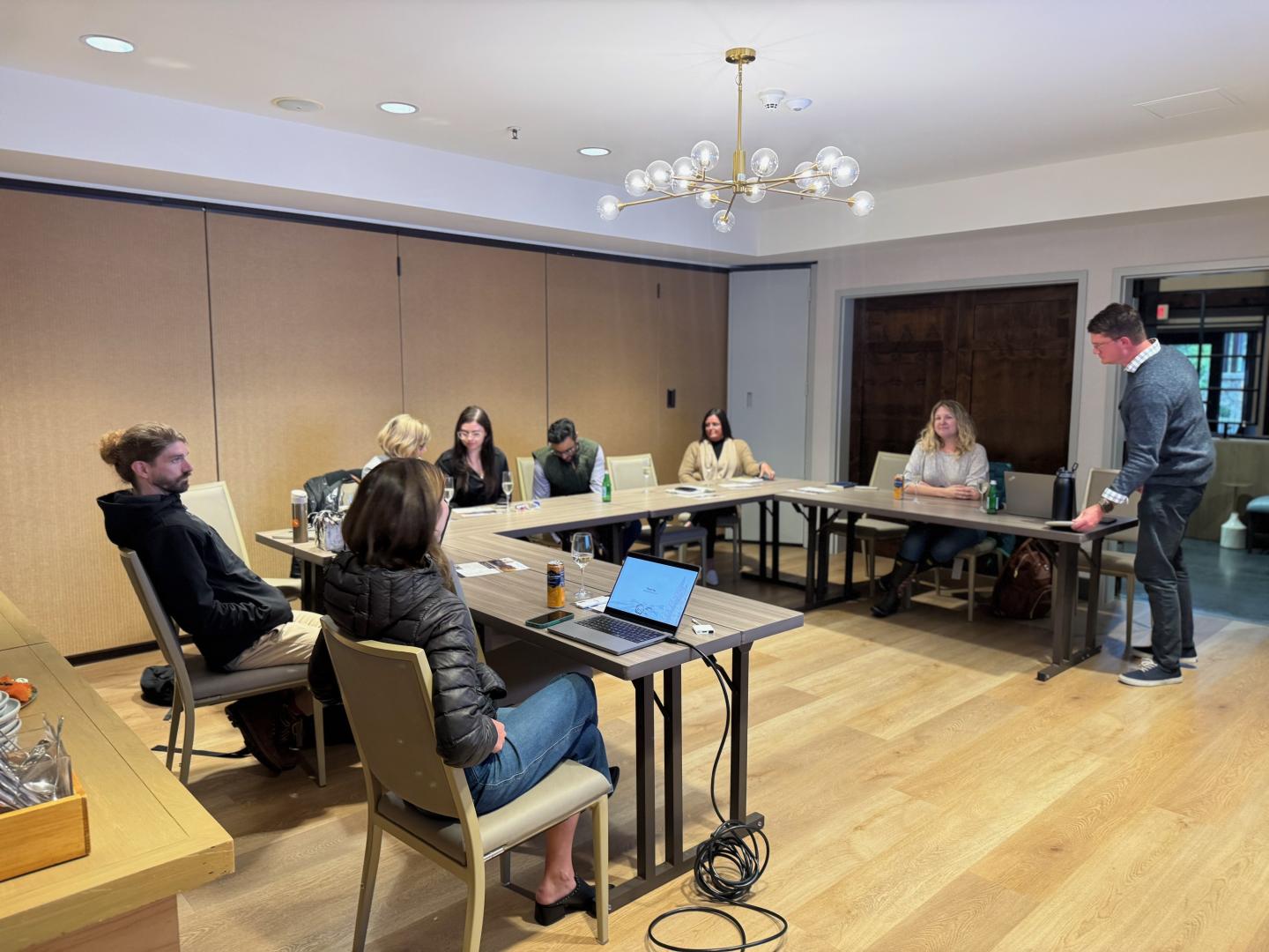 Meeting room with people seated around a U-shaped table, one person standing.