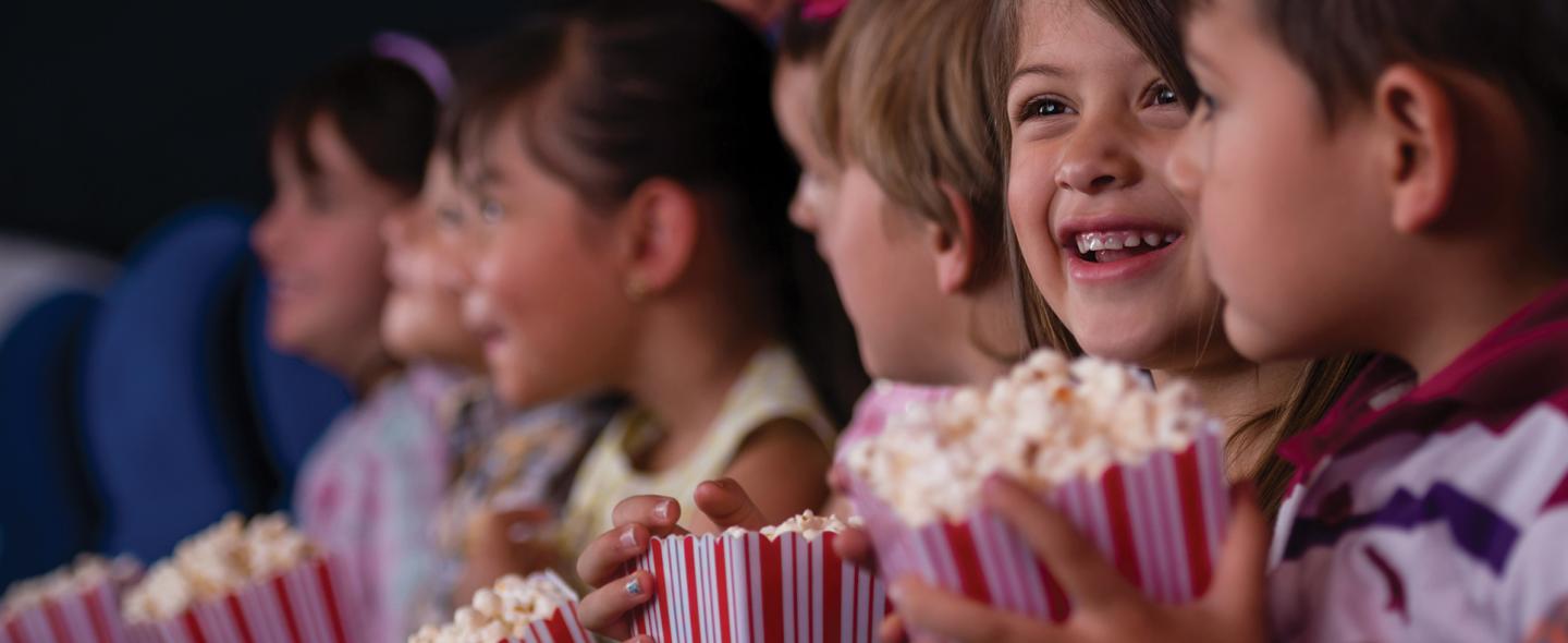 Children smiling with popcorn in a theater row.
