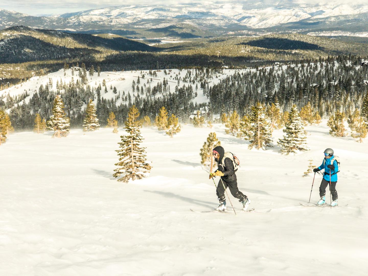 Two people snowshoeing in a snowy mountain landscape with trees.