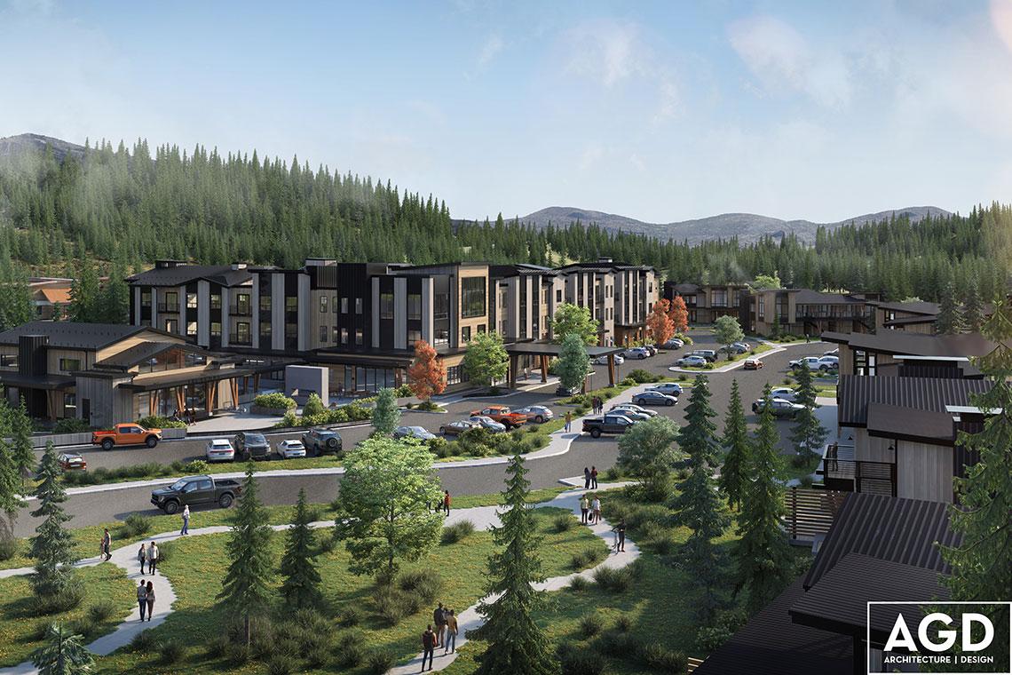 Modern buildings with parking, surrounded by trees and mountains under a blue sky.