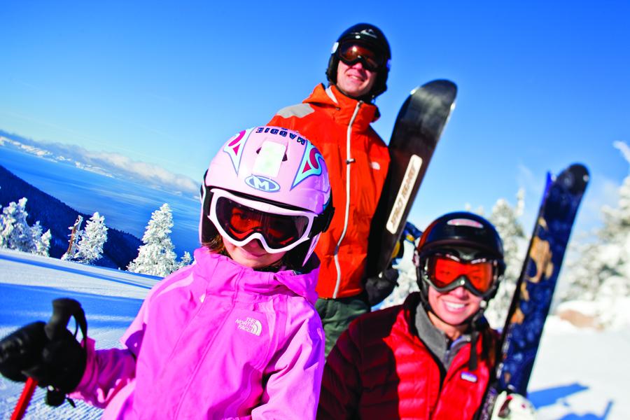 Three people in ski gear on a snowy mountain under a clear blue sky.