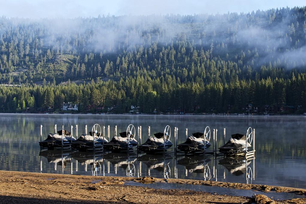 Boats docked on a calm lake with a misty forest background.