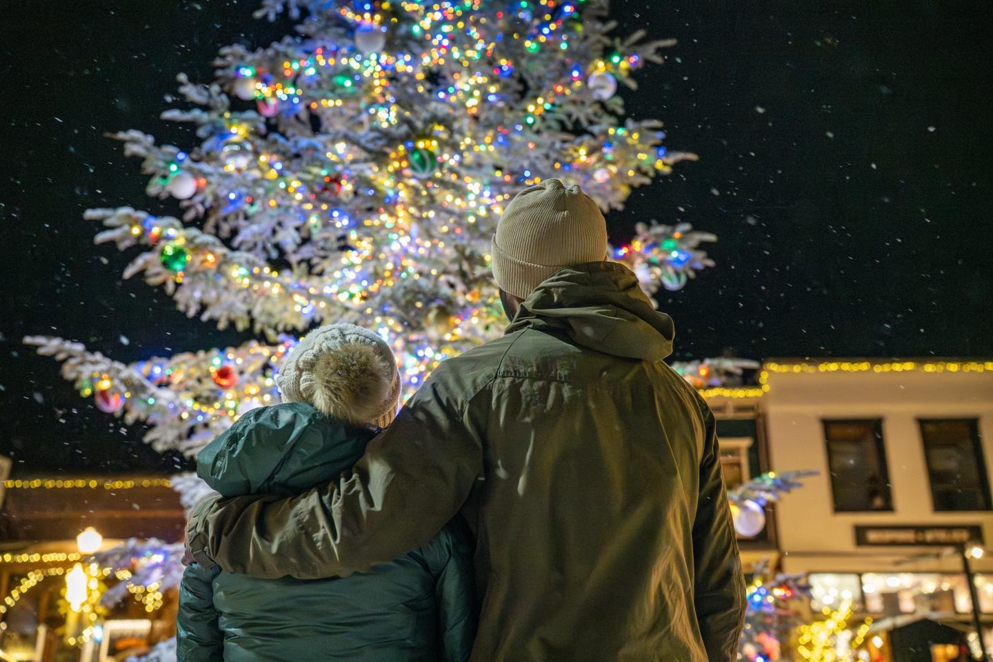 Couple embraces under a lit Christmas tree at night.