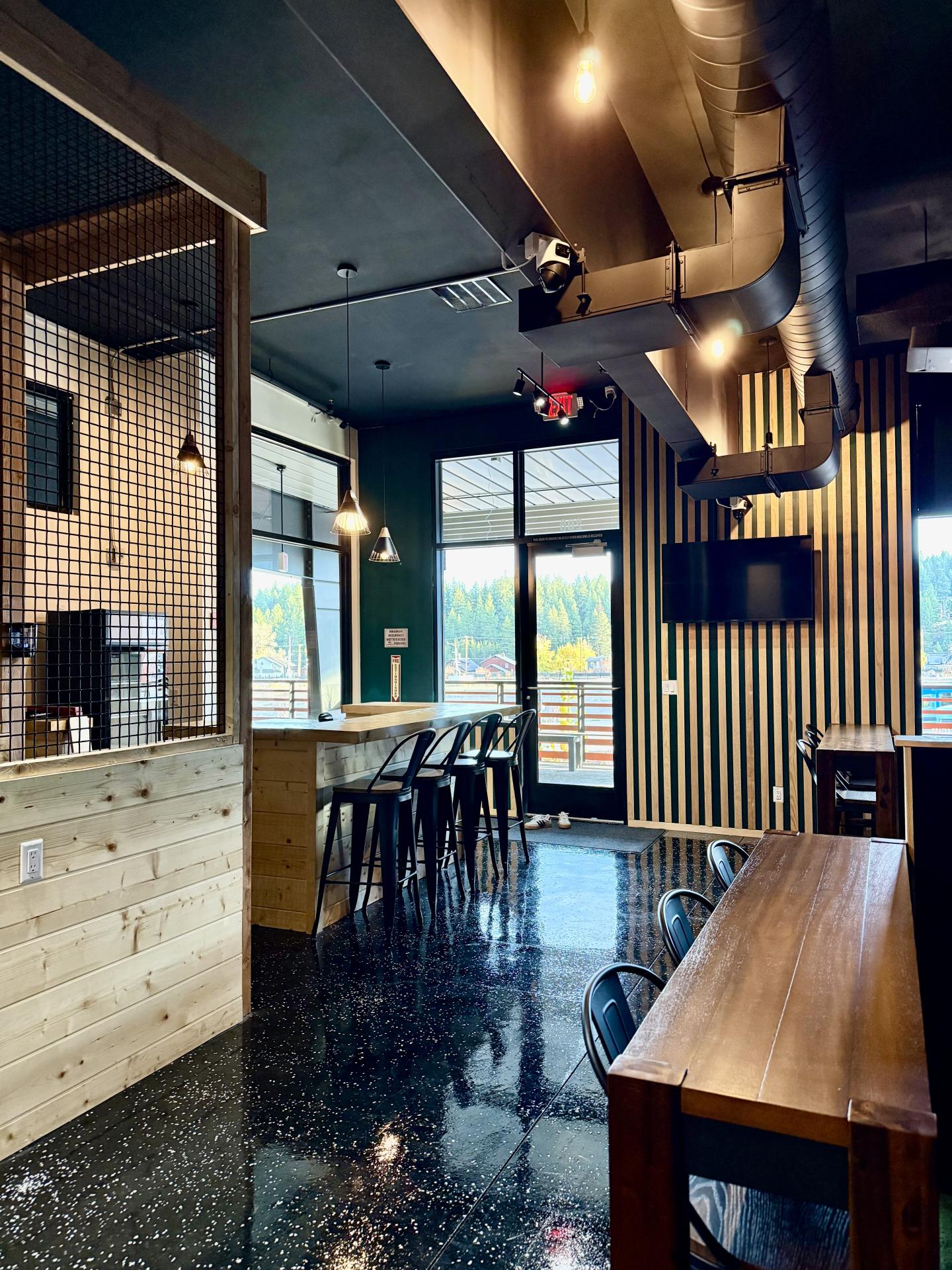 Airy cafe interior with wooden tables, black chairs, and large windows.