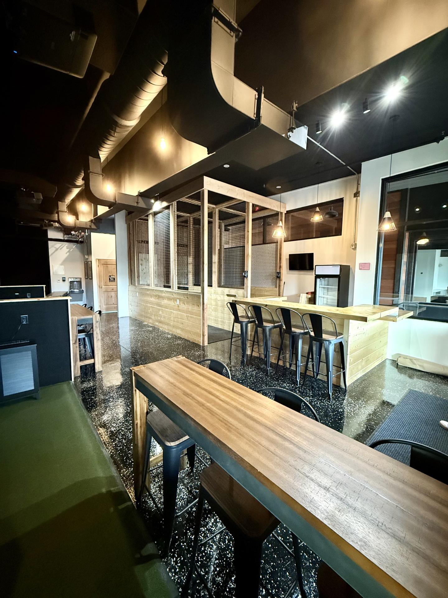 Modern cafe interior with high wooden tables and stools, dim lighting.