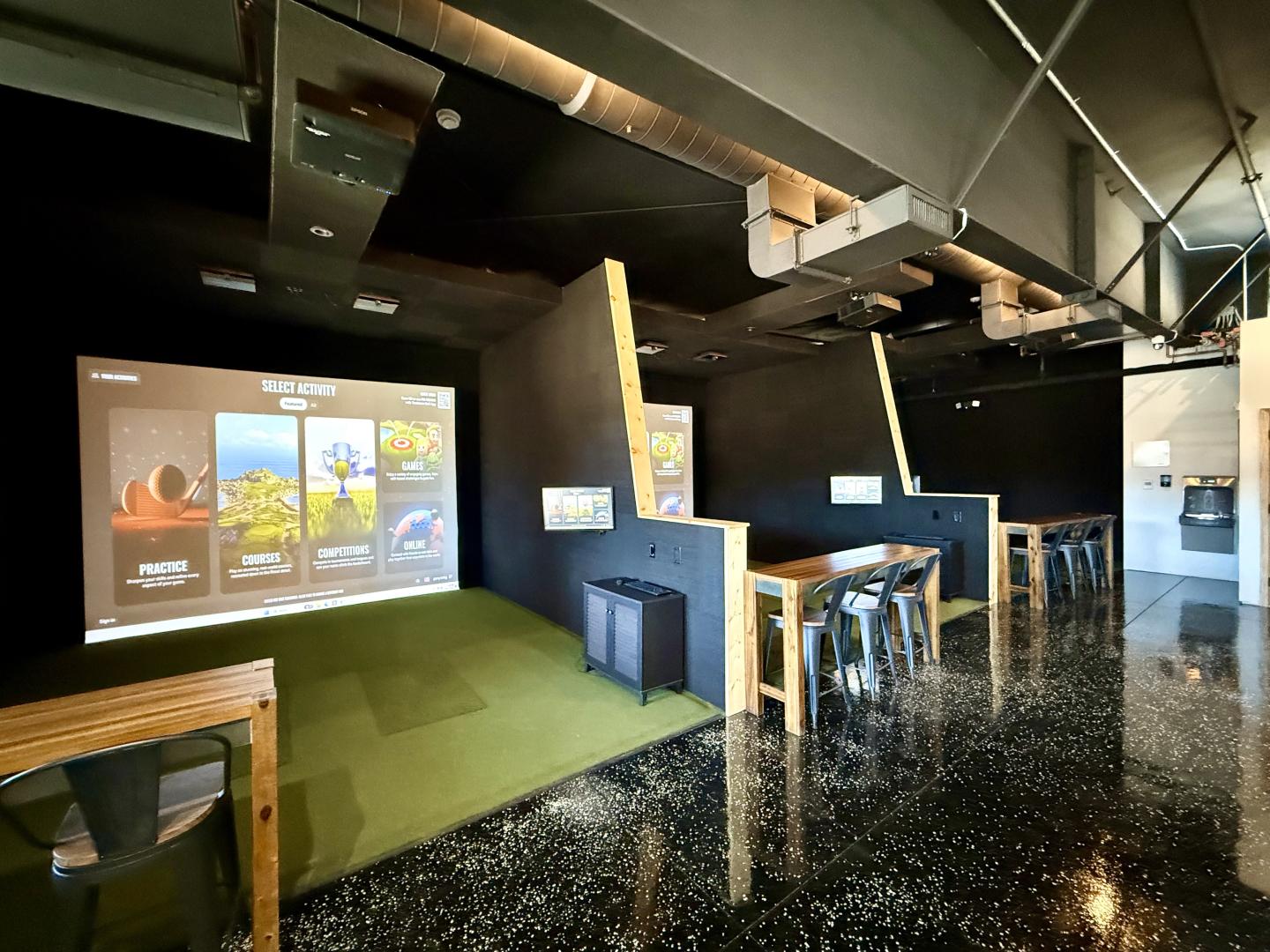 Modern indoor golf simulator setup with chairs and tables on a polished floor.