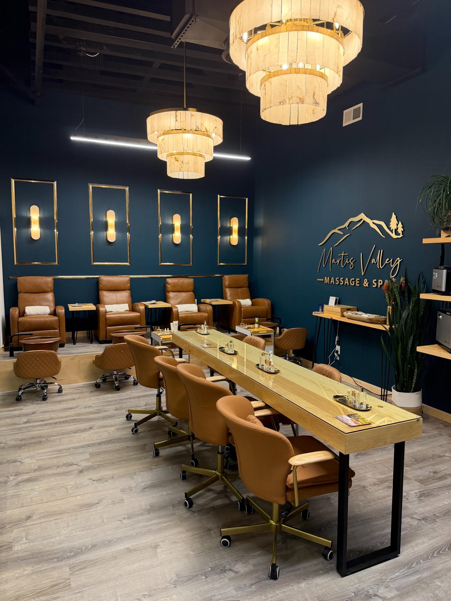Nail salon interior with navy walls, tan chairs, and gold accents under chandeliers.