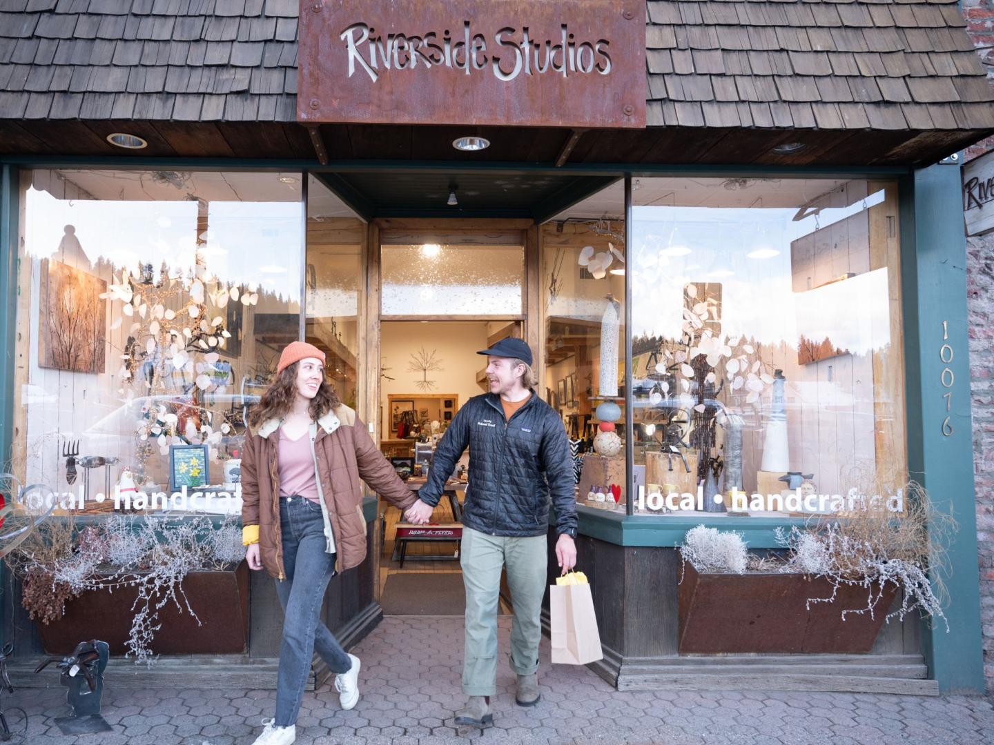 Couple holding hands, exiting a storefront with large windows.