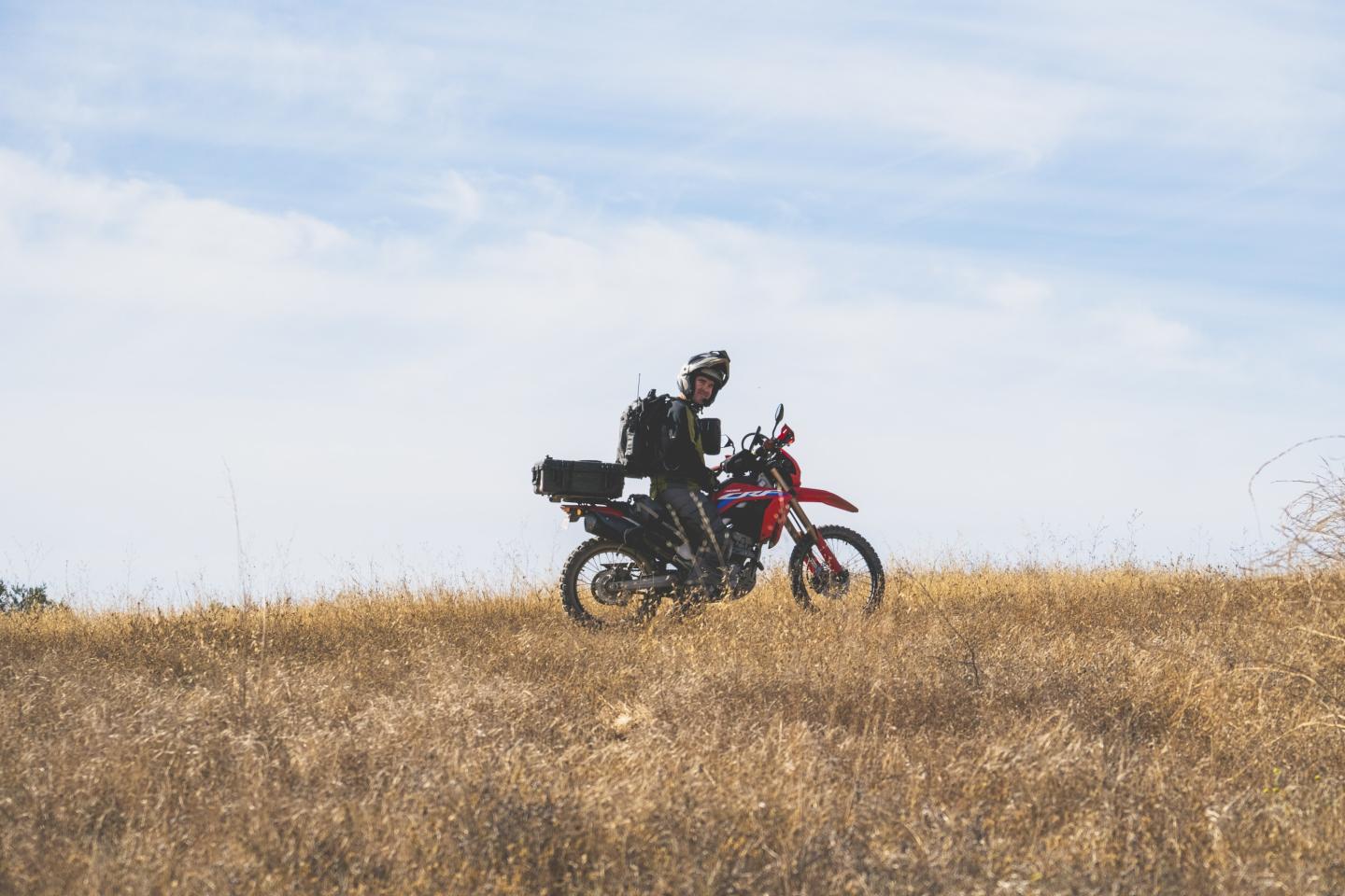 Motorcyclist on a red bike riding through a dry grassy field.