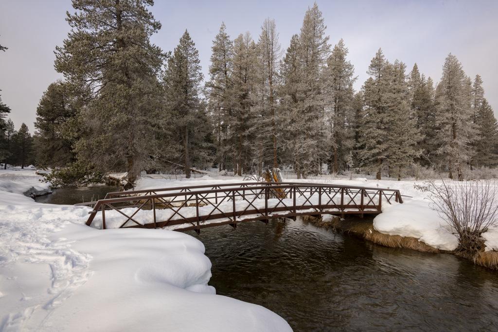 Snowy bridge over a river, surrounded by frost-covered trees.