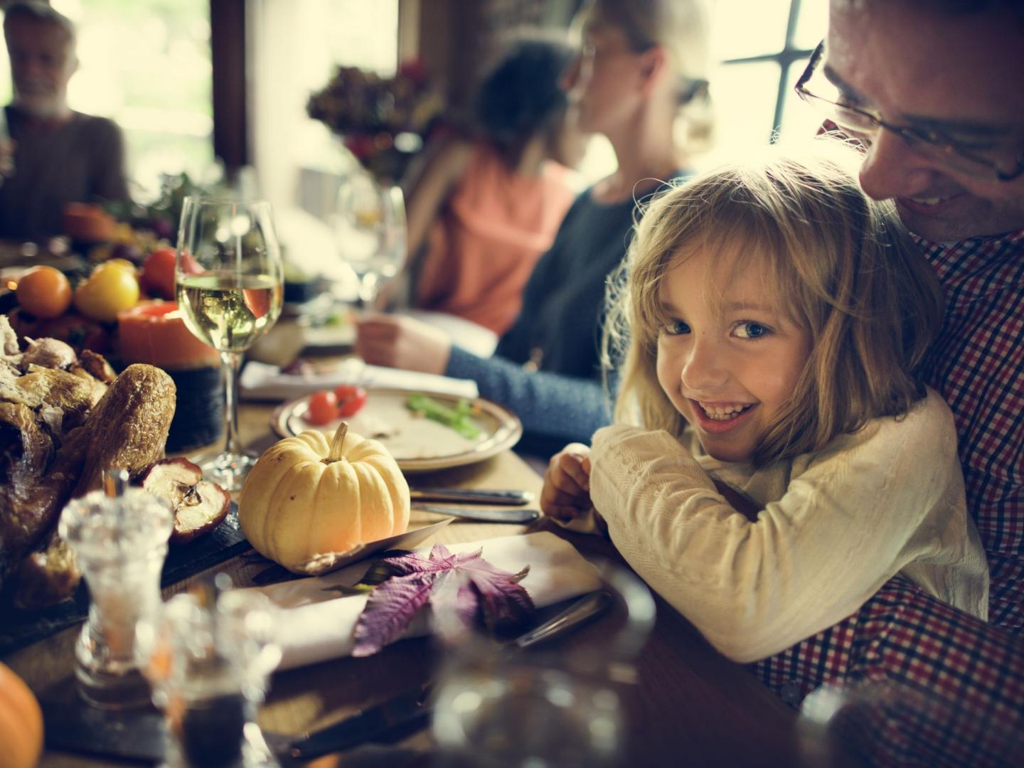 Family dining around a table, child smiling with an adult, autumn decorations present.