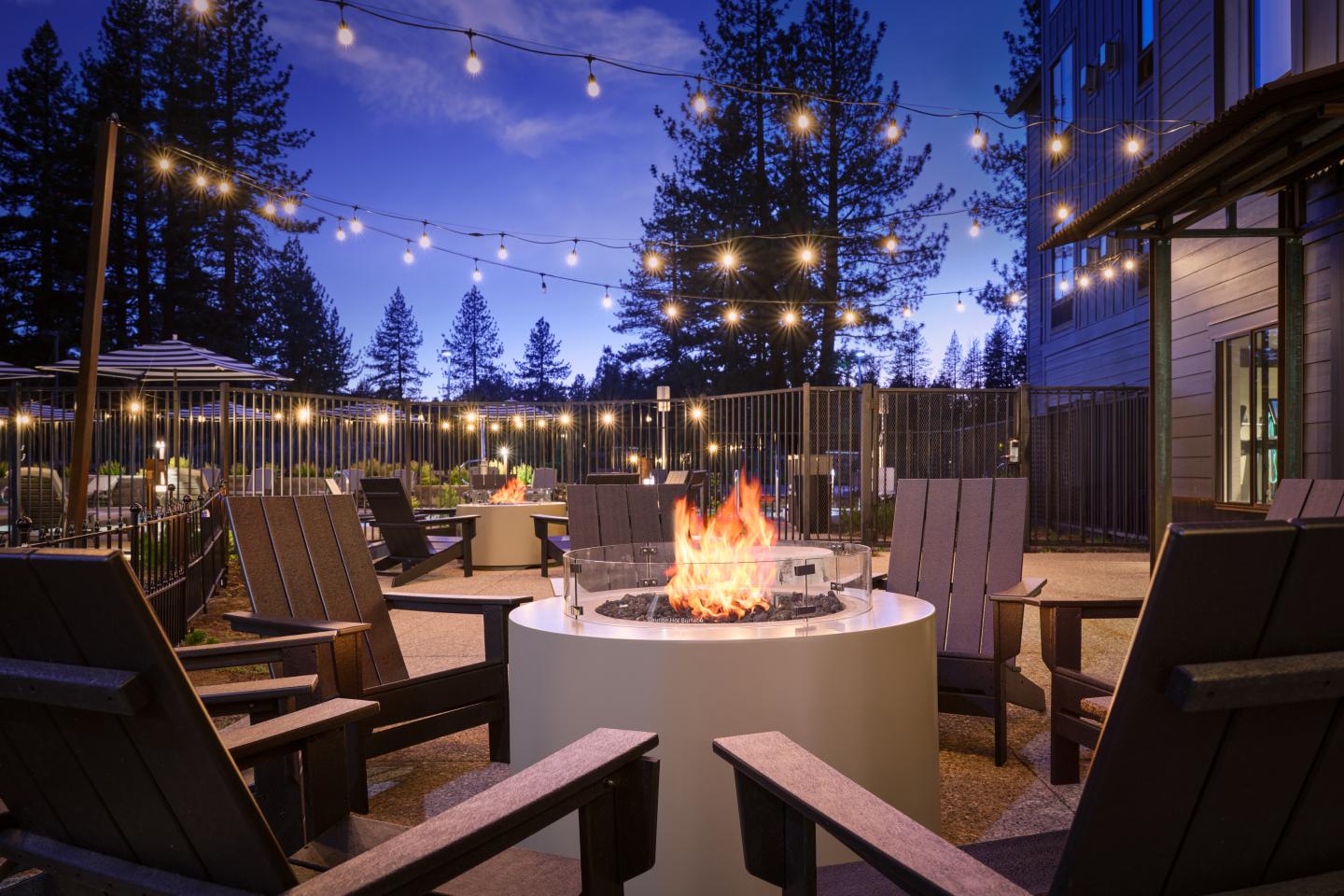 Cozy outdoor fire pit with chairs and string lights at dusk.