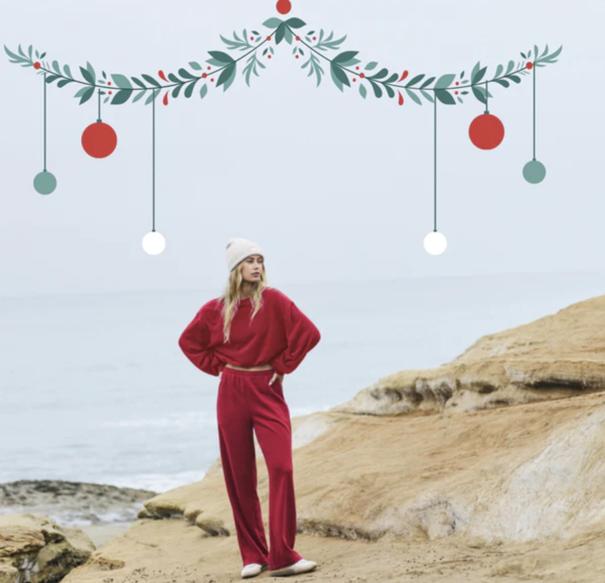 Woman in red outfit stands on rocky beach with festive garland above.