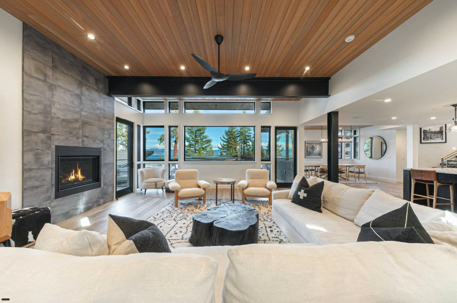 Modern living room with fireplace, large windows, and light wood ceiling.