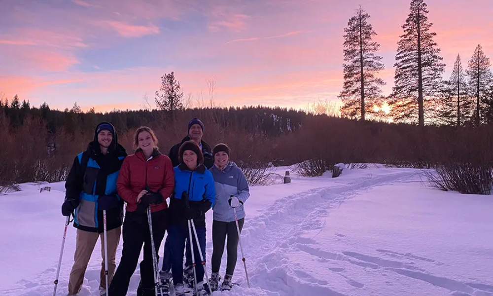 Group snowshoeing at sunset, snowy path and trees in background.
