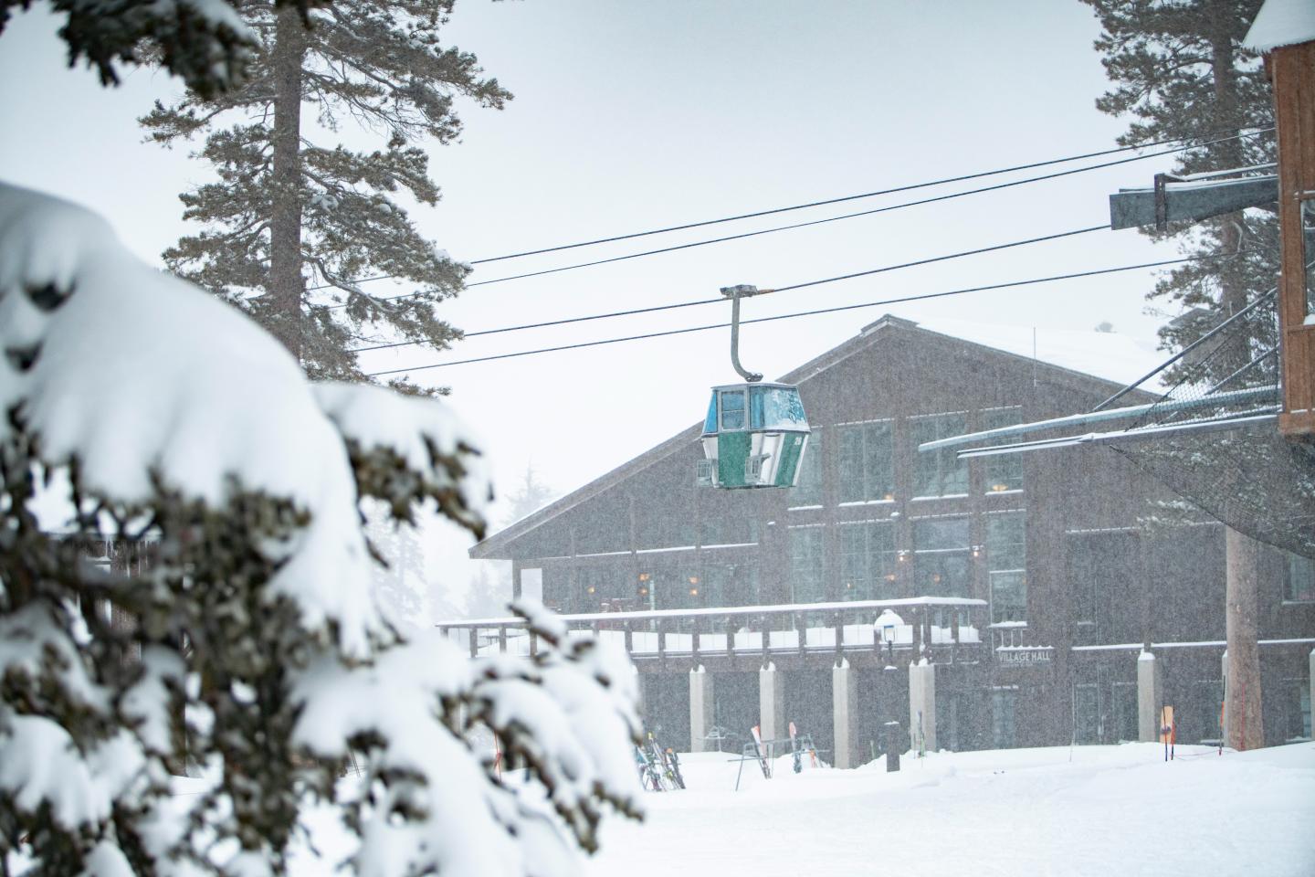Snowy lodge with ski lift, pine trees, and falling snow.
