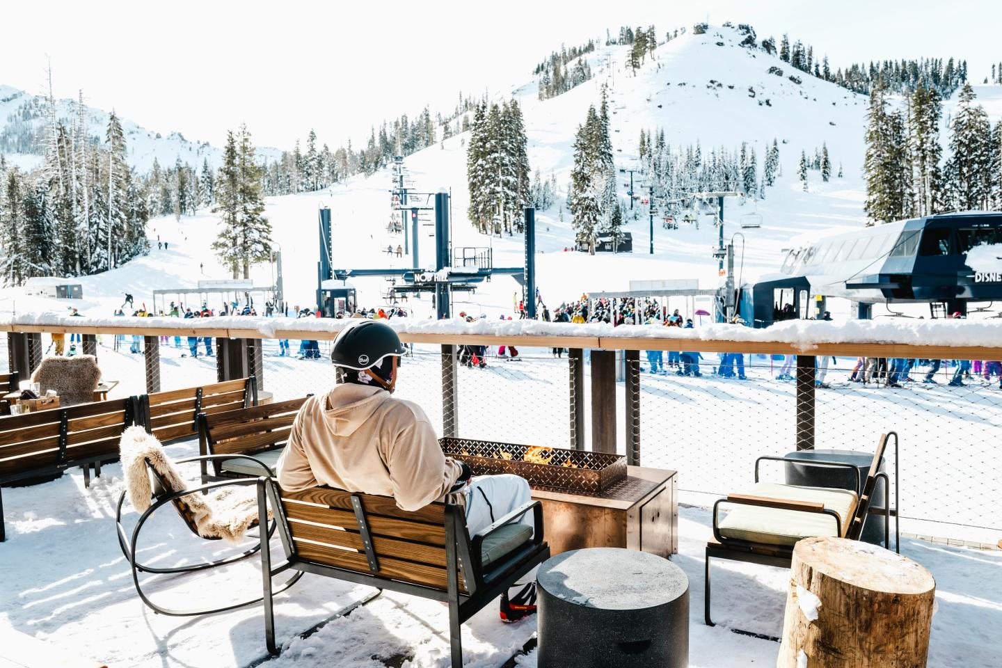 Man in warm clothes sitting by outdoor fireplace at snowy ski resort.